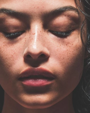 Close-up portrait of a woman with freckles and closed eyes photographed by Dan Jackson.