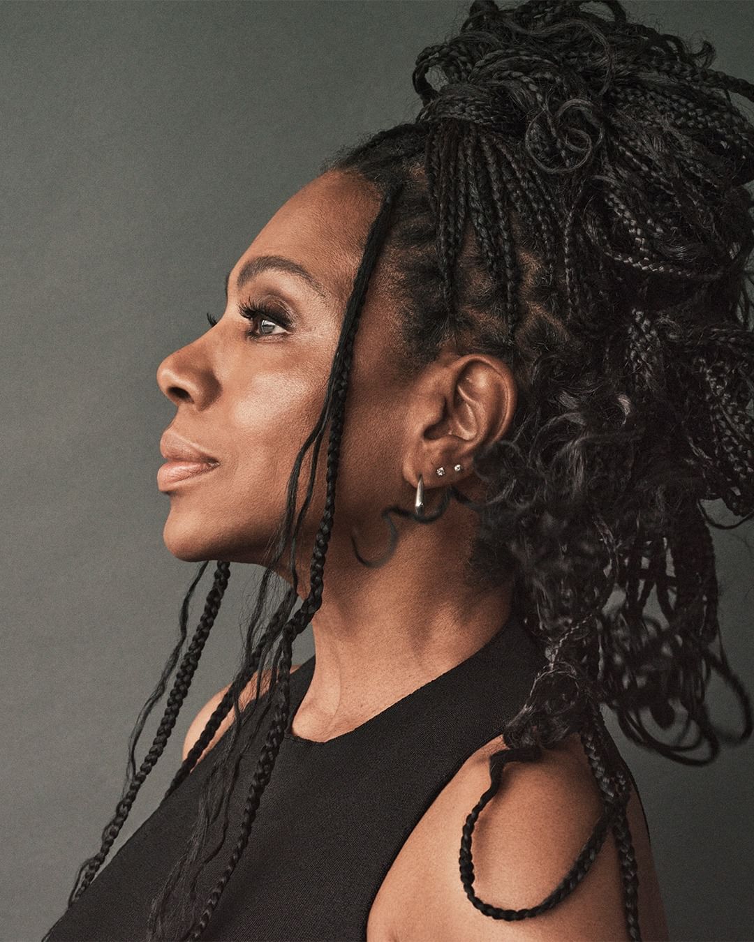 Profile portrait of a Black woman with braided hair wearing a black top against a grey studio backdrop by photographer Dan Jackson.