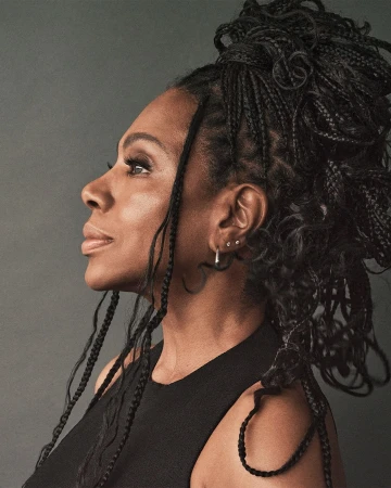 Profile portrait of a Black woman with braided hair wearing a black top against a grey studio backdrop by photographer Dan Jackson.