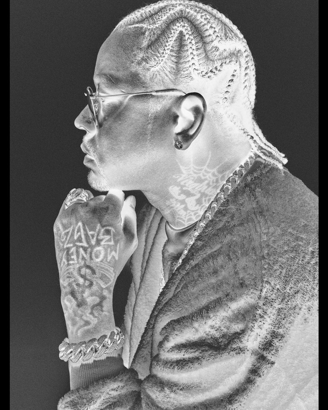 Close-up, inverted, portrait of an adult male with cornrow braids, glasses, and tattoos, wearing a robe, against a black background.