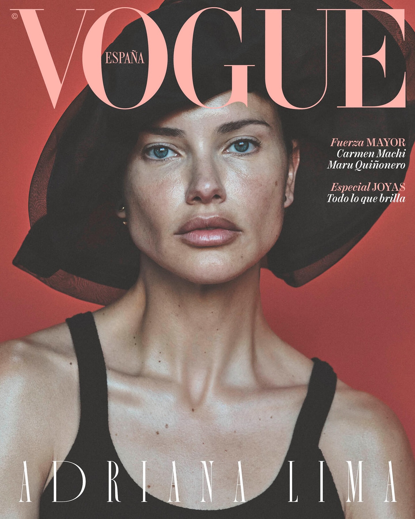 Fashion magazine cover featuring Adriana Lima wearing a black hat and tank top against a red backdrop, with 'Vogue España' at the top.