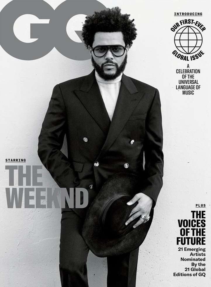 The Weeknd poses on a GQ magazine cover in a black double-breasted suit and glasses, holding a wide-brimmed black hat against a gray backdrop.