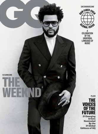 The Weeknd poses on a GQ magazine cover in a black double-breasted suit and glasses, holding a wide-brimmed black hat against a gray backdrop.
