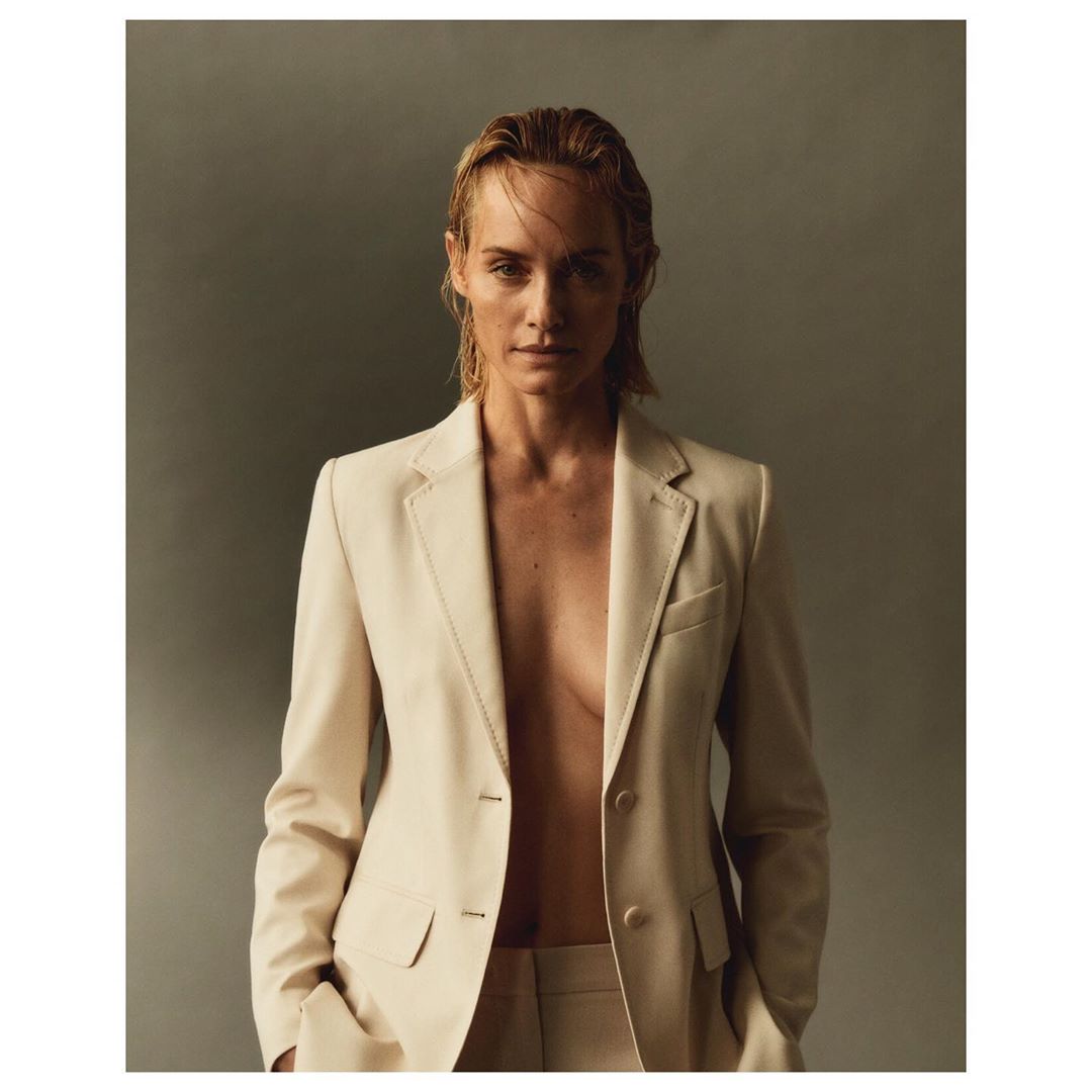 Fashion portrait of a woman wearing a beige suit jacket and pants, posing in front of a neutral grey background in a studio.