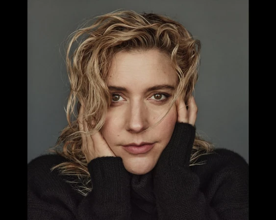 Close-up portrait of a woman with wet blonde hair holding her face in her hands wearing a black sweater against a grey background