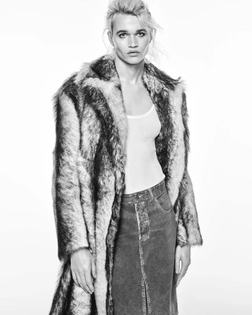 Model wearing a textured faux-fur coat over a white tank top and denim skirt against a bright white background.