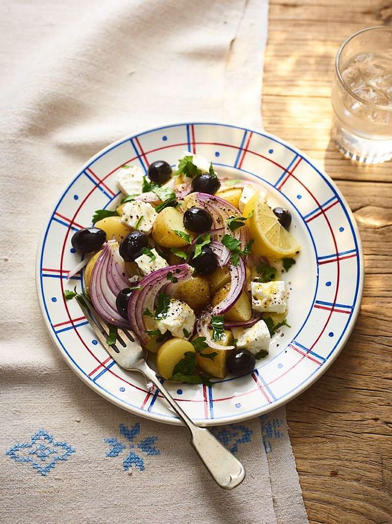 Overhead shot of potato salad on a patterned plate with a fork, featuring potatoes, olives, red onions, and feta cheese.