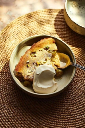 Overhead shot of a slice of cake on a round plate with cream and a spoon, set atop a woven mat under natural lighting.
