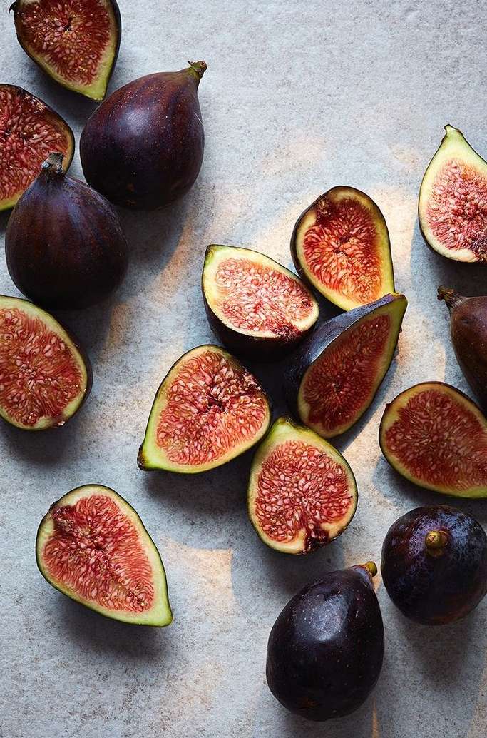 Overhead shot of halved and whole ripe figs scattered on a textured light gray surface, creating a visually appealing food still life.