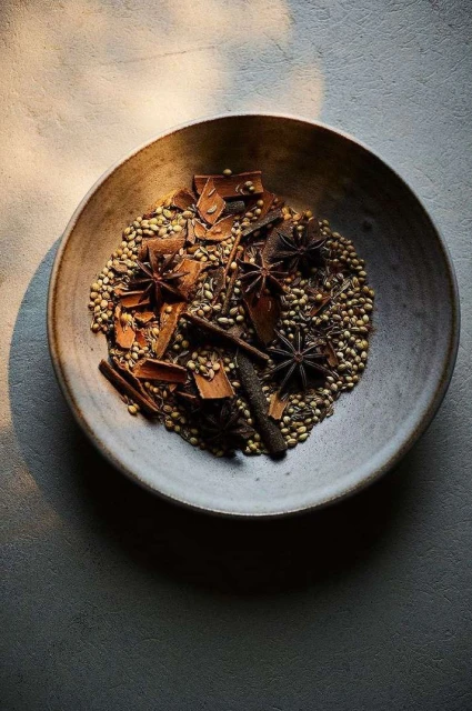 Overhead shot of a rustic bowl filled with an assortment of aromatic spices including star anise and cinnamon sticks.