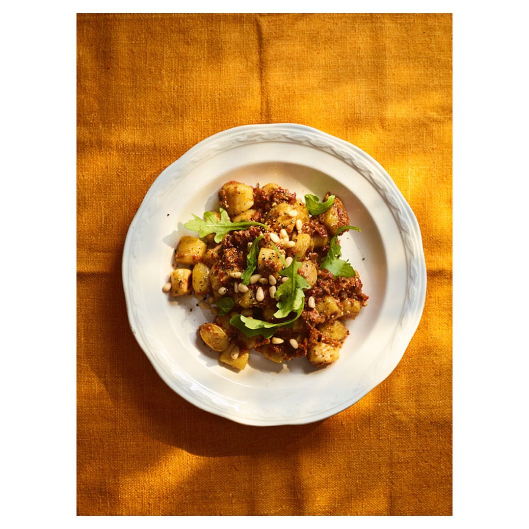 Overhead shot of gnocchi with pesto on a white plate atop a textured orange linen tablecloth, bathed in warm, natural light.