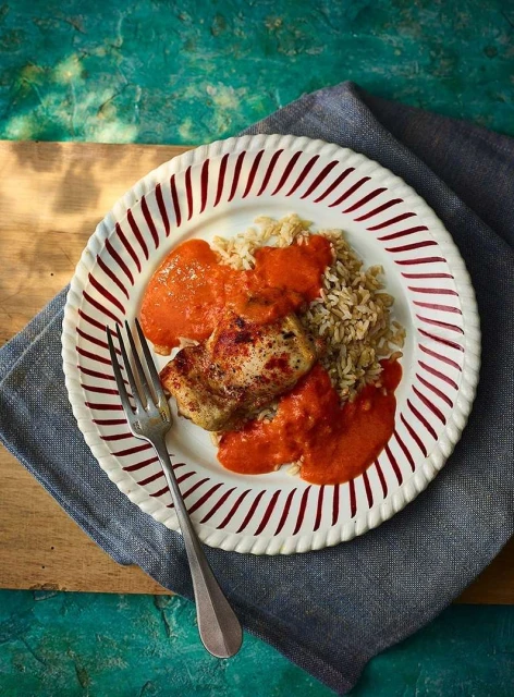 Overhead shot of a plate with chicken, rice, and red sauce on a wooden board with a gray cloth and blue textured background.