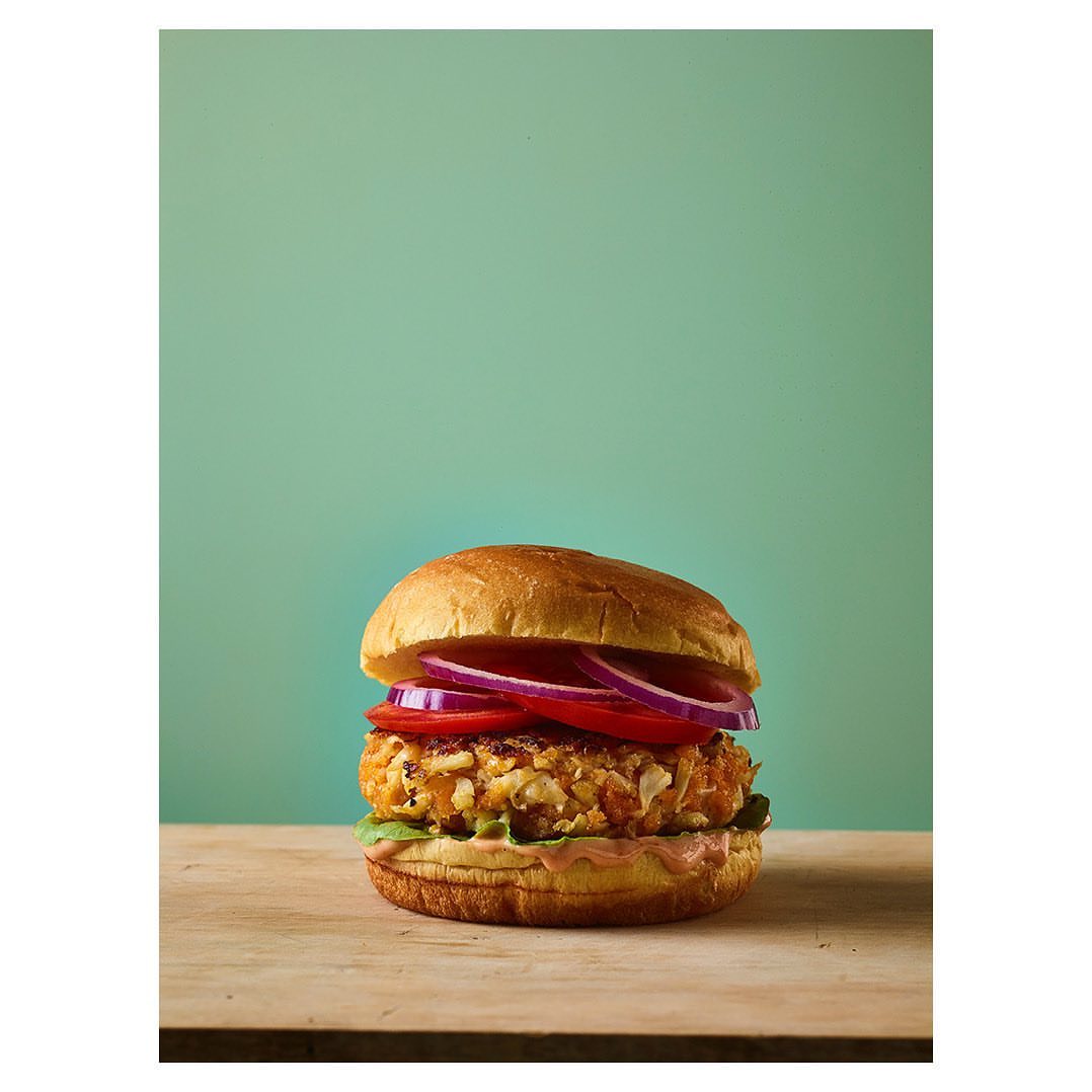 Eye-level studio shot of a veggie burger featuring a patty, lettuce, sliced red onions, and a sesame seed bun on a wood surface.