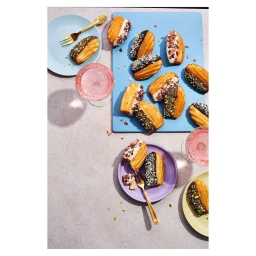 Top-down view of glazed madeleines, pastel plates, and cocktail glasses on a stone surface by Dan Jones