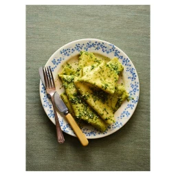 Plate of pasta with green herb sauce and cutlery resting on a textured fabric surface, photographed by Dan Jones