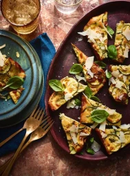 Overhead food photography of sliced zucchini frittata with parmesan and basil on a dark red platter by Dan Jones.