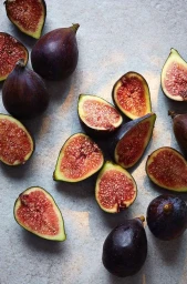 Top-down view of whole and halved purple figs scattered across a light grey textured stone surface.