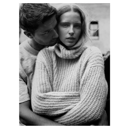 Black and white portrait of a woman in a chunky turtleneck sweater embraced by a man in London.