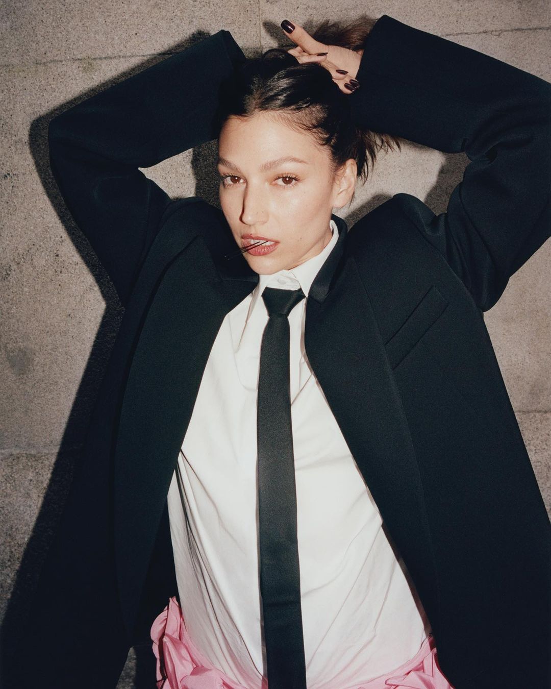Woman in an oversized black blazer, white shirt, and black tie holding her hair up, photographed by Dan Martensen.