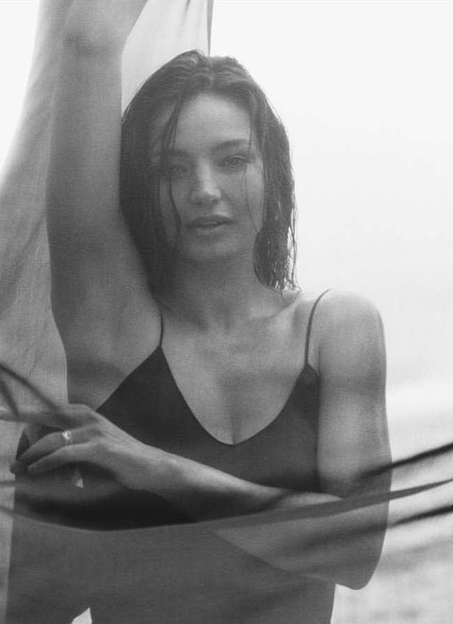 Monochromatic portrait of a woman in black top, gazing at the camera, posing with a translucent veil in an outdoor setting.
