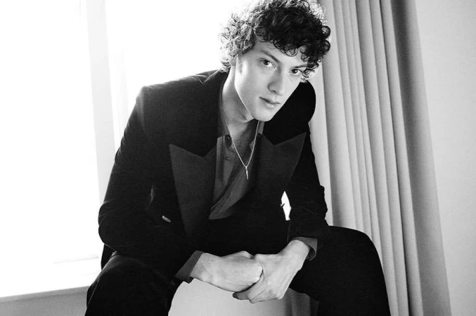 Monochrome portrait of a young man with curly hair wearing a dark blazer and a thin pendant necklace in London by Dan Martensen.