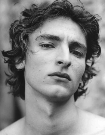 Close-up black and white portrait of a young man with curly dark hair looking directly at the camera.