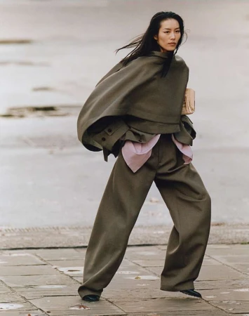 Model in olive green wool cape and wide-leg trousers walking outdoors on a paved street in London, photographed by Dan Martensen.