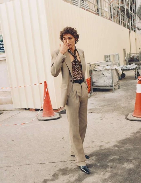 Stylish adult male in suit with leopard print shirt in outdoor urban setting with orange traffic cones on neutral concrete ground.
