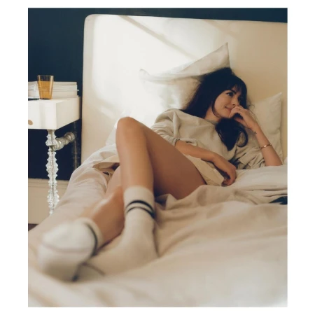 Woman in crewneck sweatshirt and white socks with stripes lying on a bed by Dan Martensen