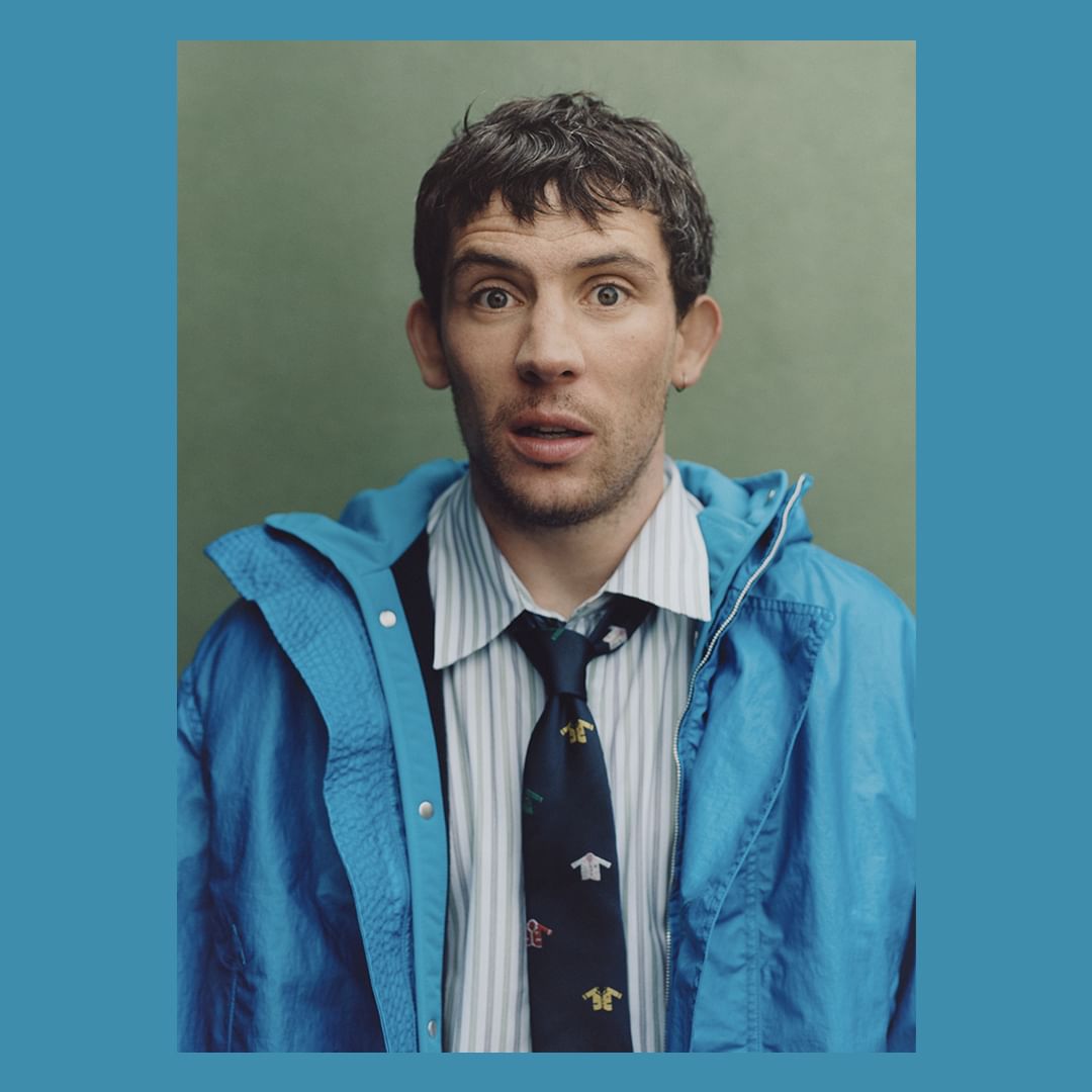 Portrait of a man wearing a blue jacket, striped shirt, and patterned tie against a green backdrop with a blue border.