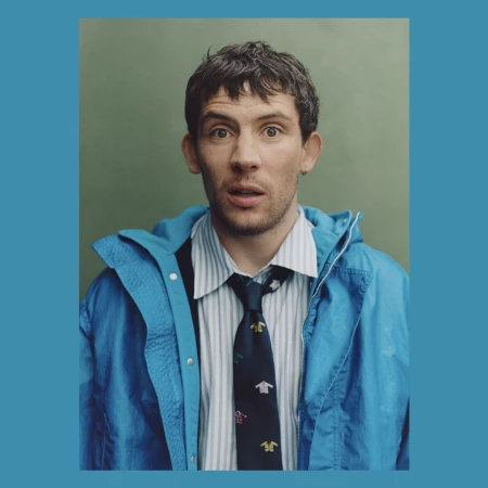 Portrait of a man wearing a blue jacket, striped shirt, and patterned tie against a green backdrop with a blue border.