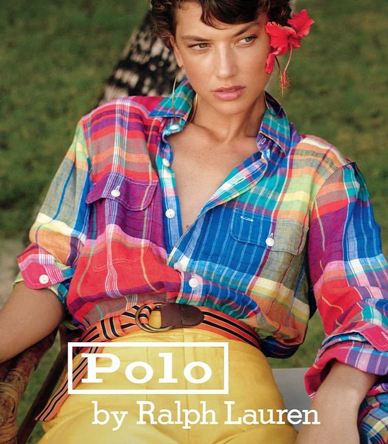 Fashion shot of a young adult woman wearing a colorful plaid shirt and yellow pants with a hibiscus flower in her hair.