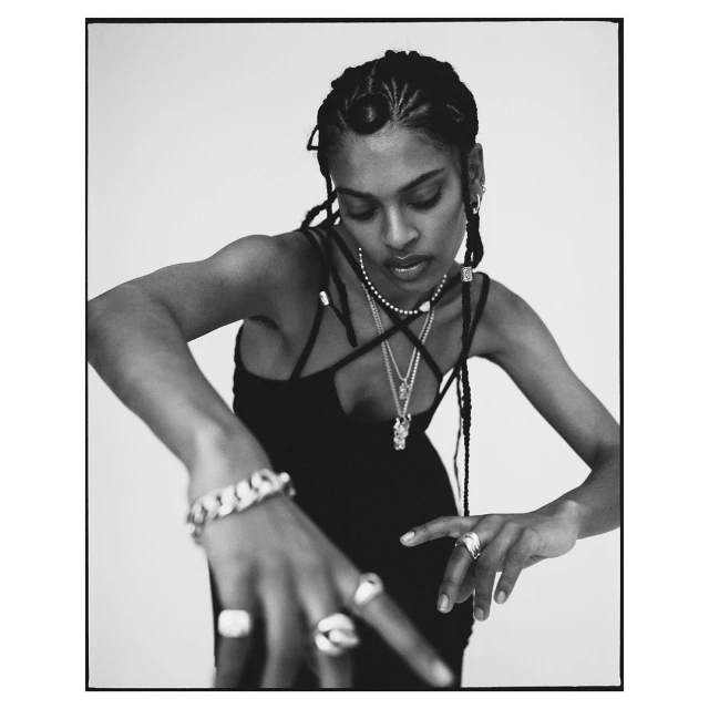 Close-up of Black woman in black dress, adorned with jewelry, captured indoors against a bright backdrop, displaying fashion and beauty elements.
