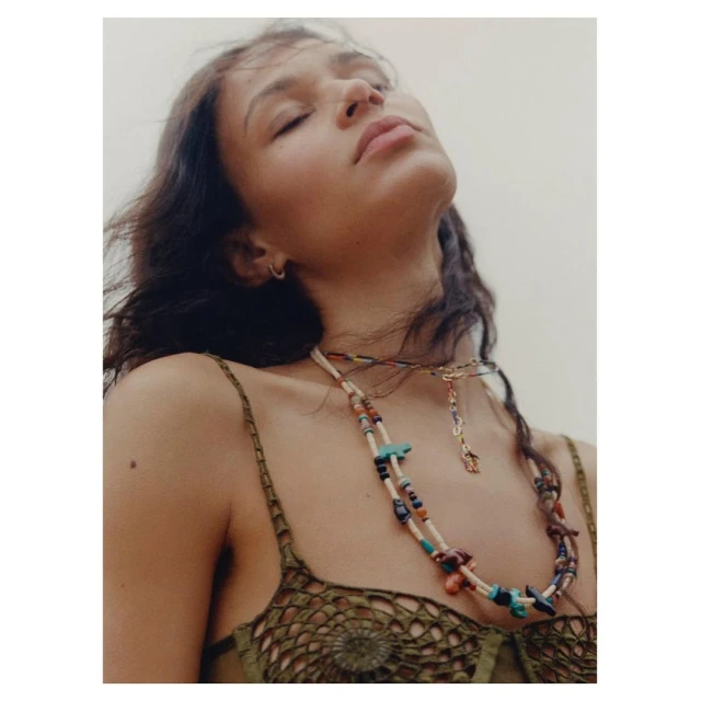 Close-up studio shot of a brunette adult female model with her eyes closed, wearing a green top and two beaded necklaces.