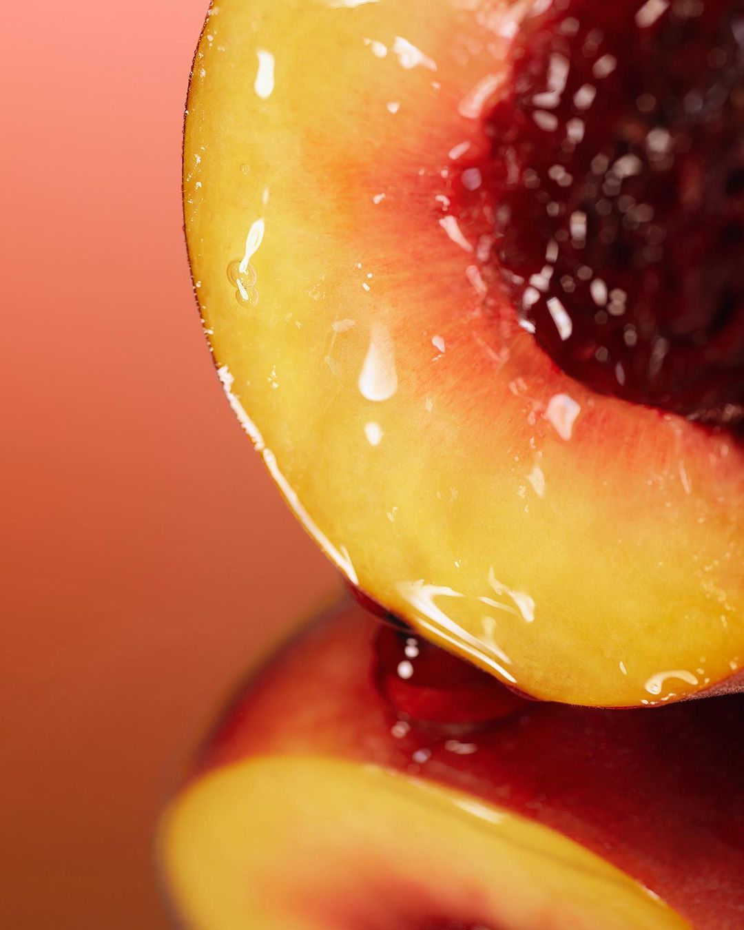 Macro close-up of a glossy peach half revealing its pit. The peach's flesh reflects light on a smooth surface against a gradient background.