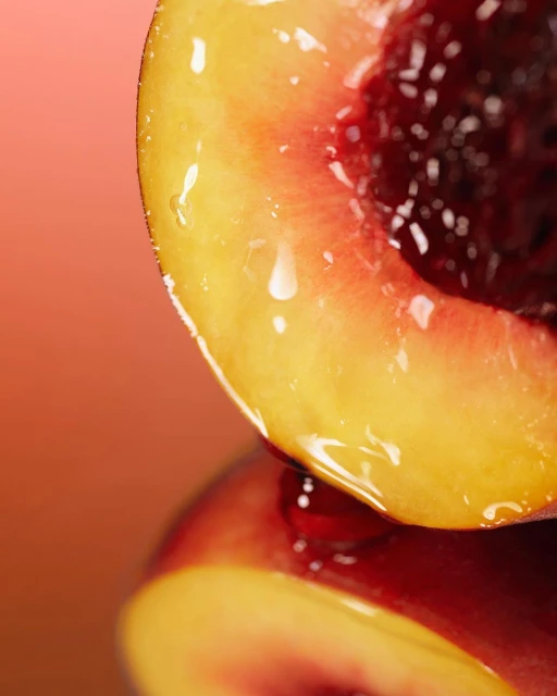 Macro close-up of a glossy peach half revealing its pit. The peach's flesh reflects light on a smooth surface against a gradient background.