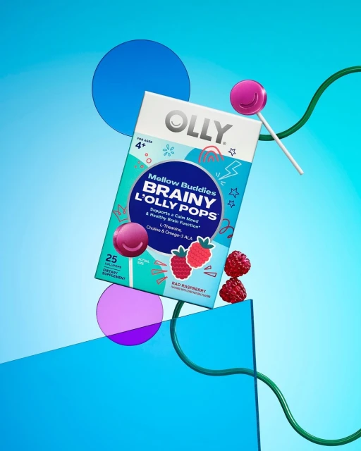 Box of Olly Brainy L'Olly Pops surrounded by lollipops, raspberries, and colorful geometric shapes on a blue gradient background.