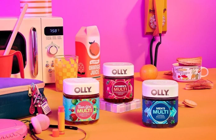 Eye-level shot of three Olly vitamin containers, an orange juice box, a microwave, and a retro yellow phone on an orange surface.