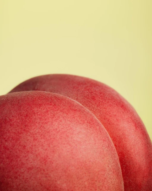 Close-up shot of two vibrant red peaches against a soft yellow background, highlighting their smooth skin and organic texture.