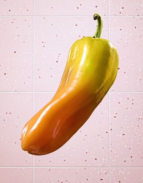 Eye-level shot of a yellow and orange bell pepper on a pink tile background, suitable for culinary or artistic applications.