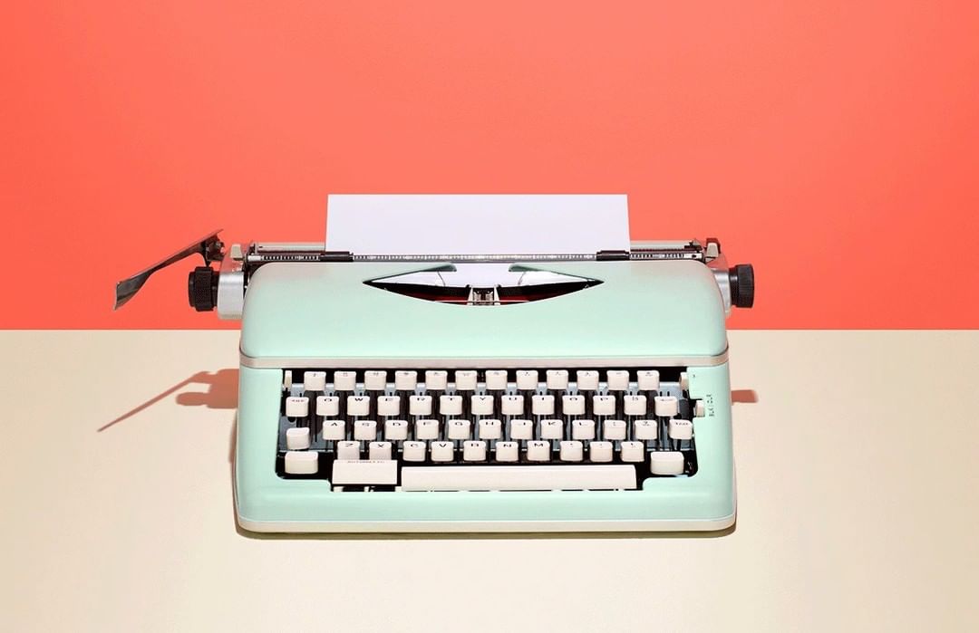 Close-up of a mint-green vintage typewriter on a tan surface against a salmon-colored background, showcasing its retro design and details.