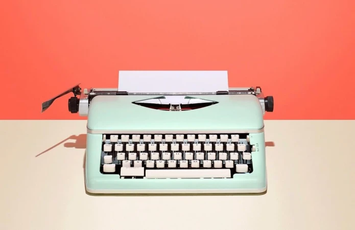 Close-up of a mint-green vintage typewriter on a tan surface against a salmon-colored background, showcasing its retro design and details.