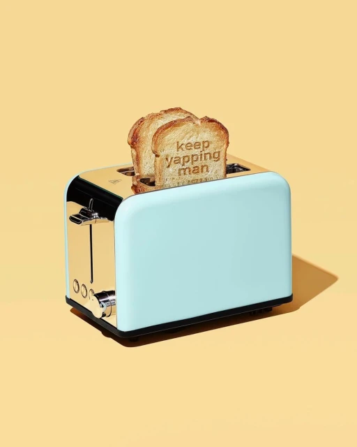 A light-blue and gold toaster features two slices of toast with stamped letters spelling out 'keep yapping man' on a yellow background.