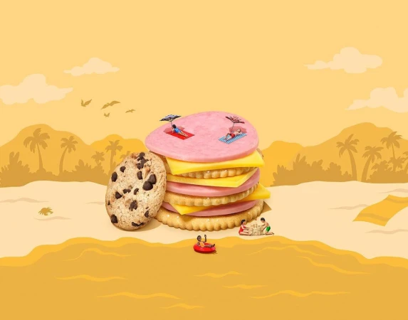 Whimsical beach scene features stacked cookies and crackers, stylized as a resort landscape with miniature sunbathers and a calm, yellow background.