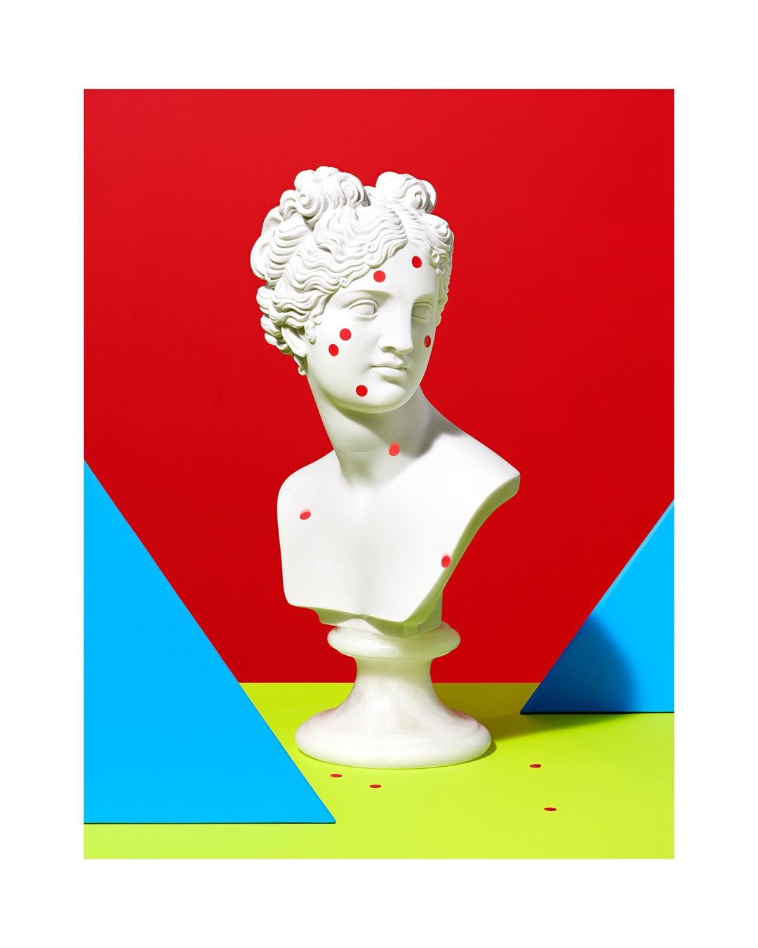 White bust sculpture with red dots on a yellow-green surface against a red backdrop and blue triangles for a pop art style.
