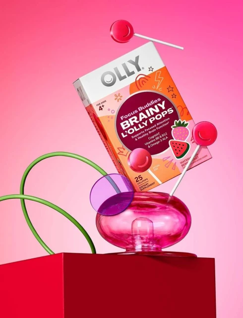 Olly Brainy L'Olly Pops box sits among lollipops and geometric shapes in a studio shot on a gradient pink backdrop.