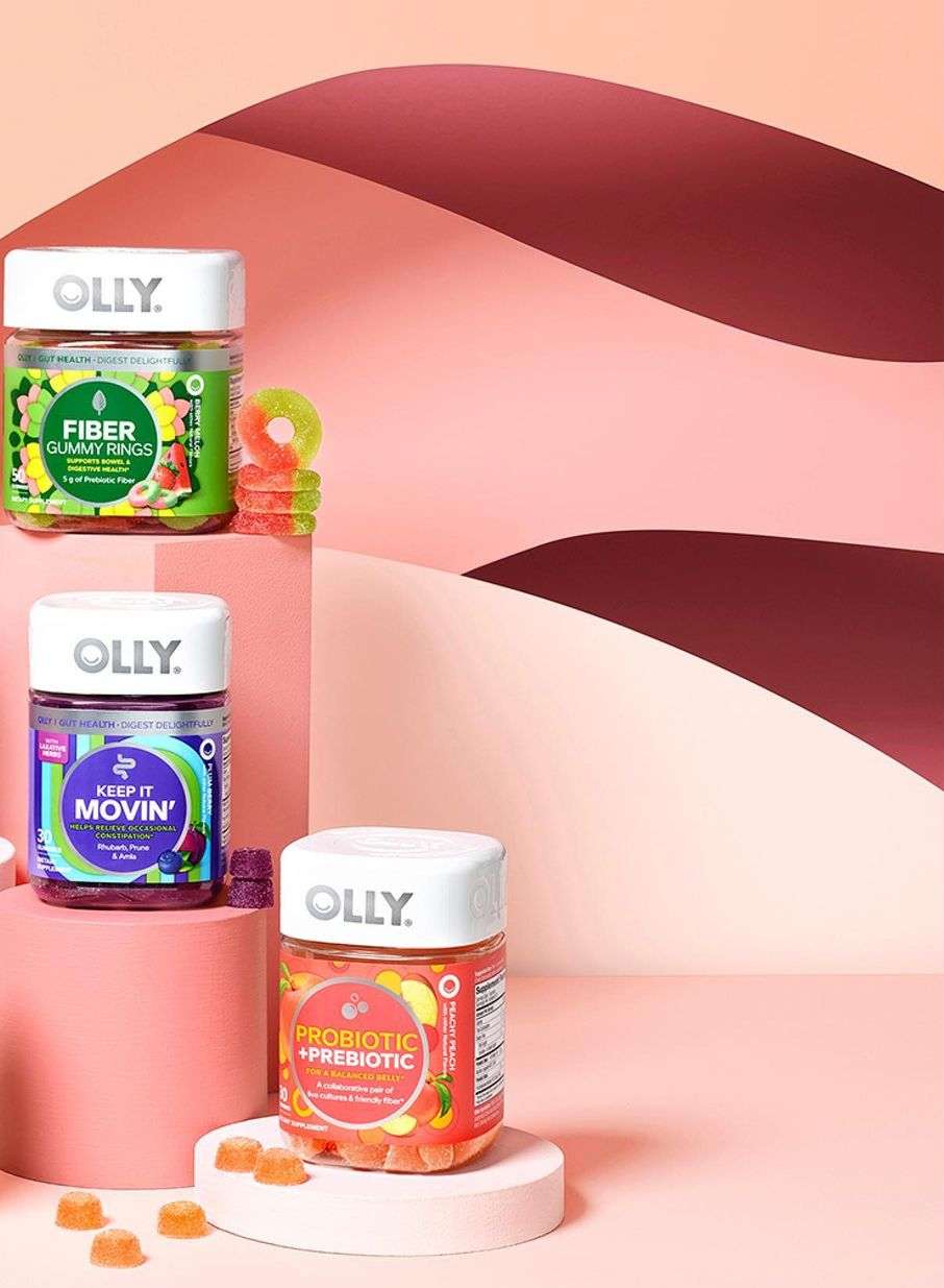 Olly brand dietary supplement gummy rings and bottles, featuring fiber, probiotic, and prebiotic varieties, on a pink background.