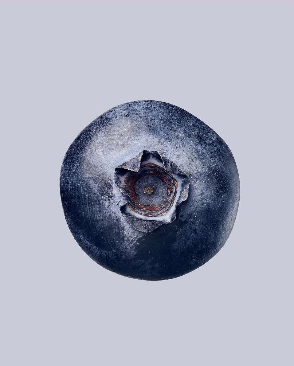 Macro photograph of a fresh blueberry with a vibrant blue hue, showcasing its natural texture and the delicate details of its stem.