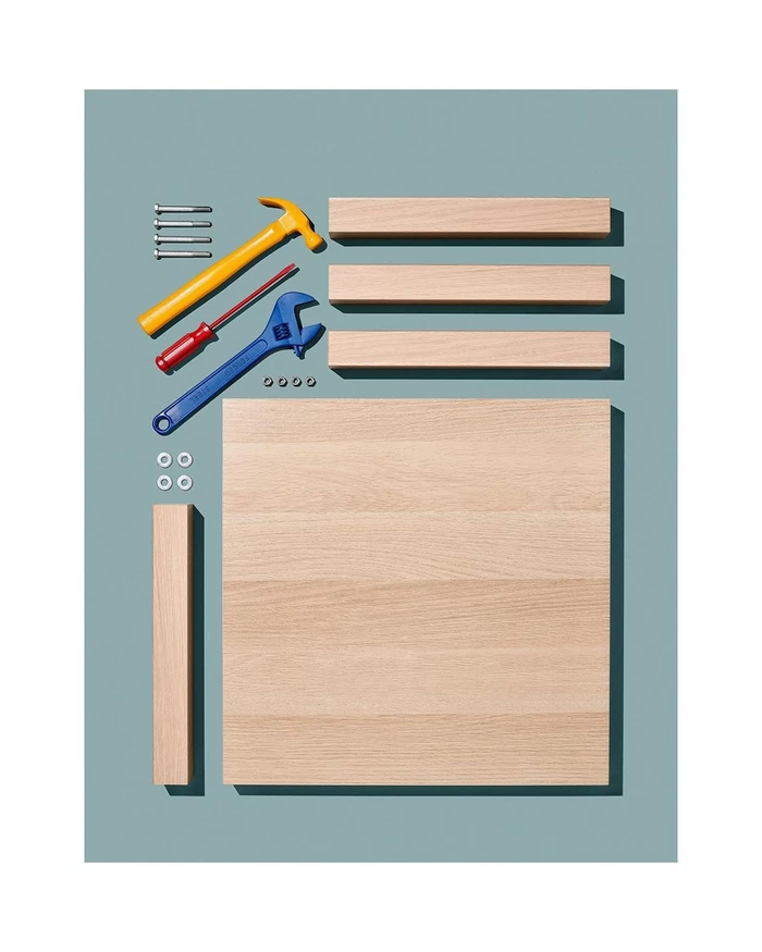Top down studio flat lay of disassembled wooden furniture parts, bolts, hammer, red screwdriver, and blue wrench.