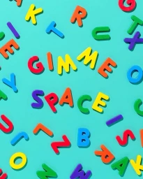 Colorful plastic magnetic letters spelling GIMME SPACE scattered on a vibrant turquoise background.